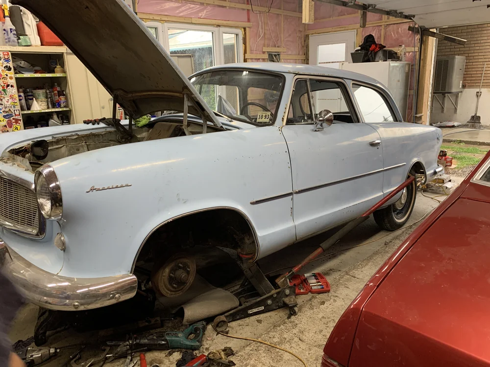 Volvo blanche en cours de travaux dans le garage, capot ouvert et roue avant retirée